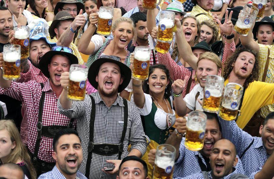 Crowd of cheering people lifting large beer mugs at Oktoberfest. - Lederhosen For Sale