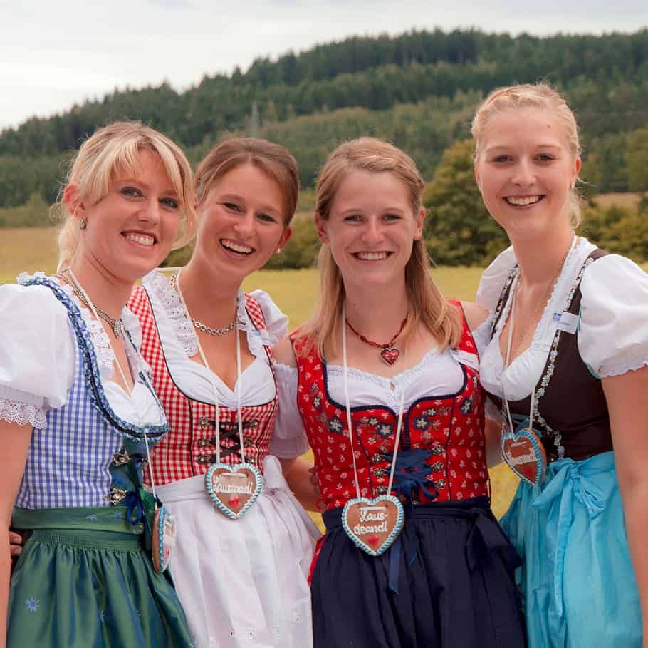 Four women smiling in colorful traditional Bavarian Dirndl dresses. - Lederhosen For Sale