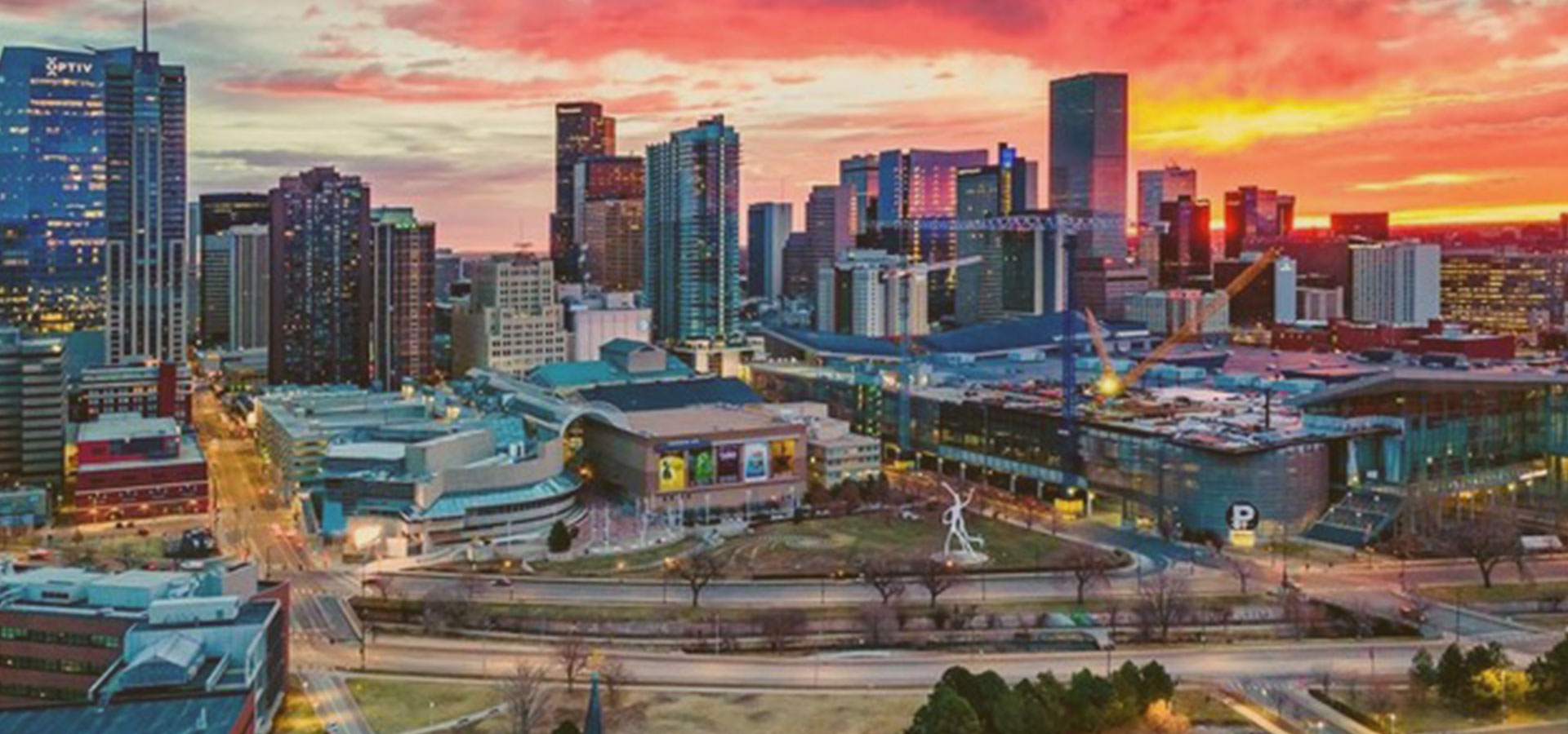 Denver skyline at sunset with illuminated skyscrapers under a vibrant orange sky - Lederhosen For Sale