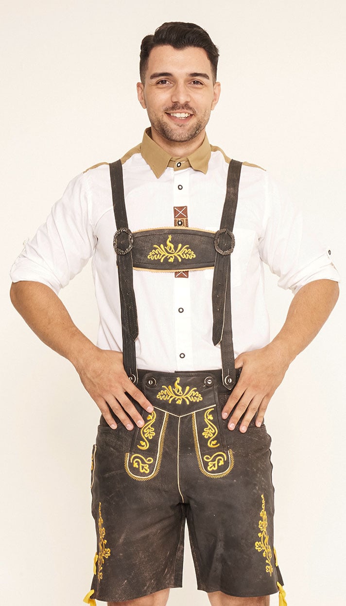 Front view of a man standing with hands on hips wearing dark brown Lederhosen with vibrant yellow embroidery and a white shirt with a tan collar. - Lederhosen For Sale