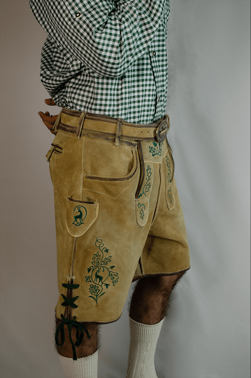 Handcrafted Oktoberfest Lederhosen in Light Gold 3 Side view of a man wearing light gold handcrafted Lederhosen shorts with detailed green stag and vine embroidery, a matching leather belt, and a green checkered shirt. - Lederhosen For Sale