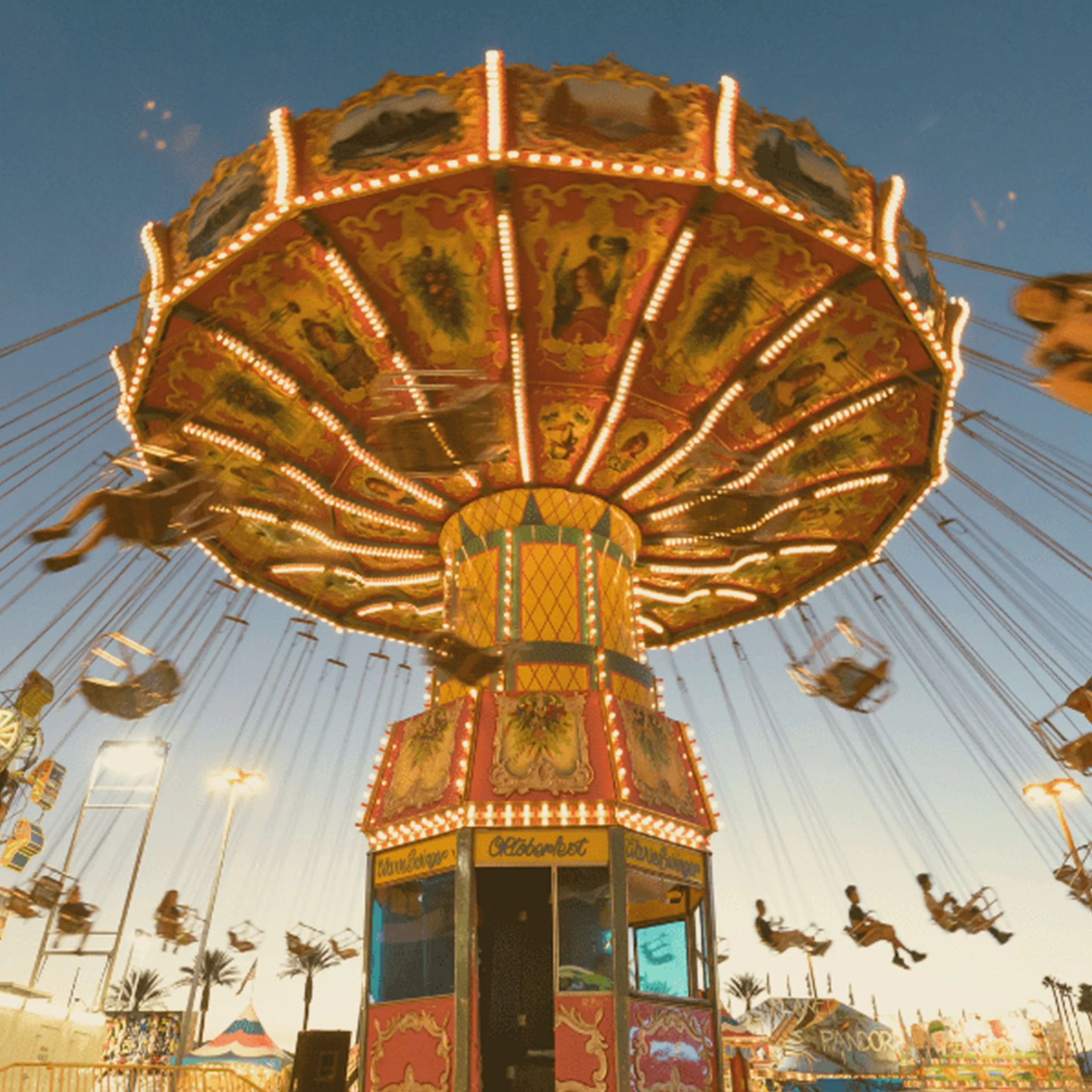 A spinning illuminated wave swinger carousel ride at an Oktoberfest event in Nevada during dusk. - Lederhosen For Sale