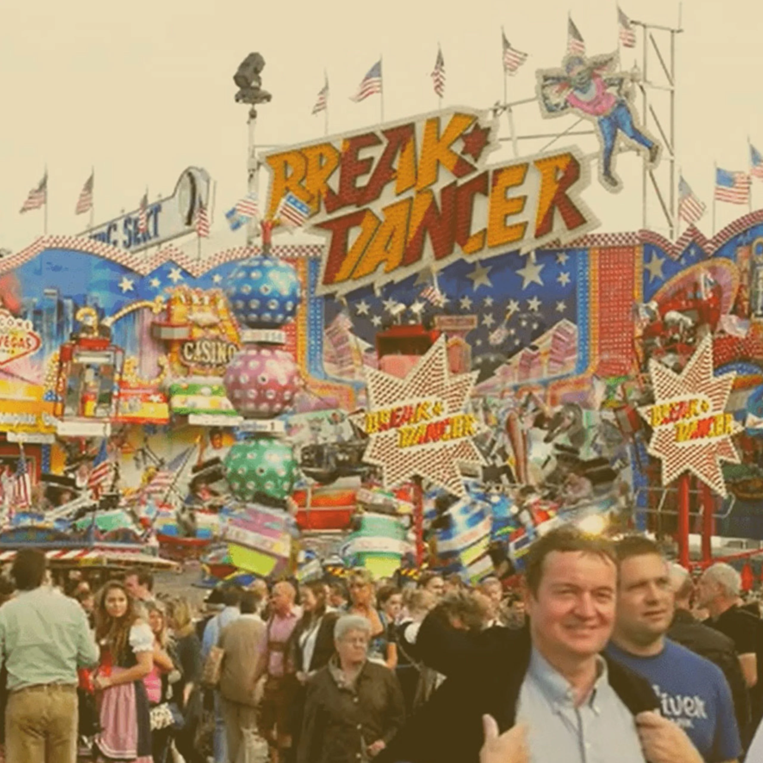 A crowded amusement park scene at an Oktoberfest event in Ohio, featuring a large "Break Dancer" spinning ride with colorful signs and flags. - Lederhosen For Sale