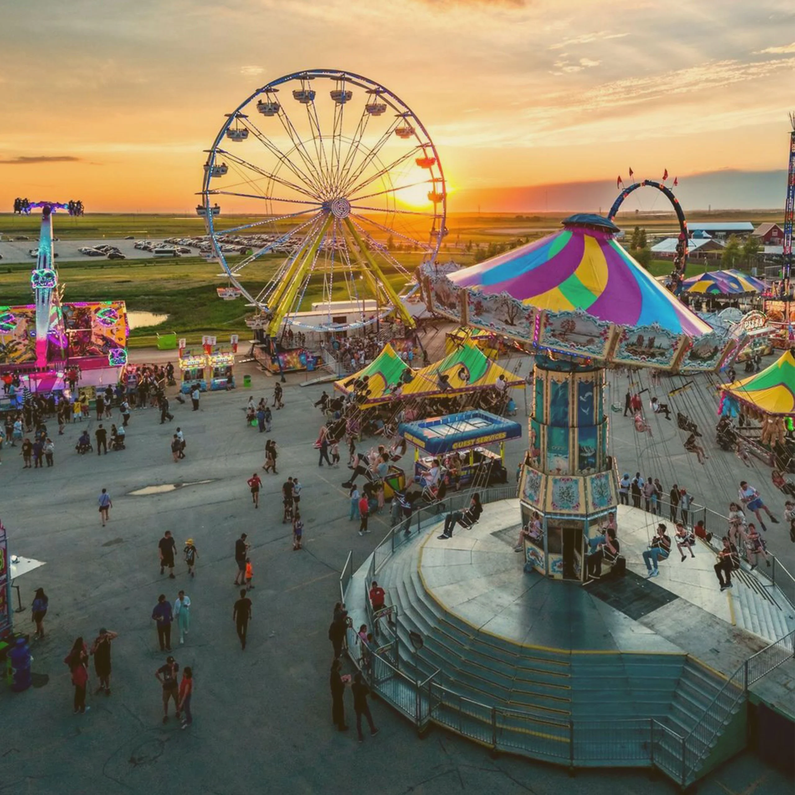 High-angle view of an amusement park at sunset during an Oktoberfest event in South Dakota, featuring a large Ferris wheel, a spinning swing ride, and green food tents. - Lederhosen For Sale