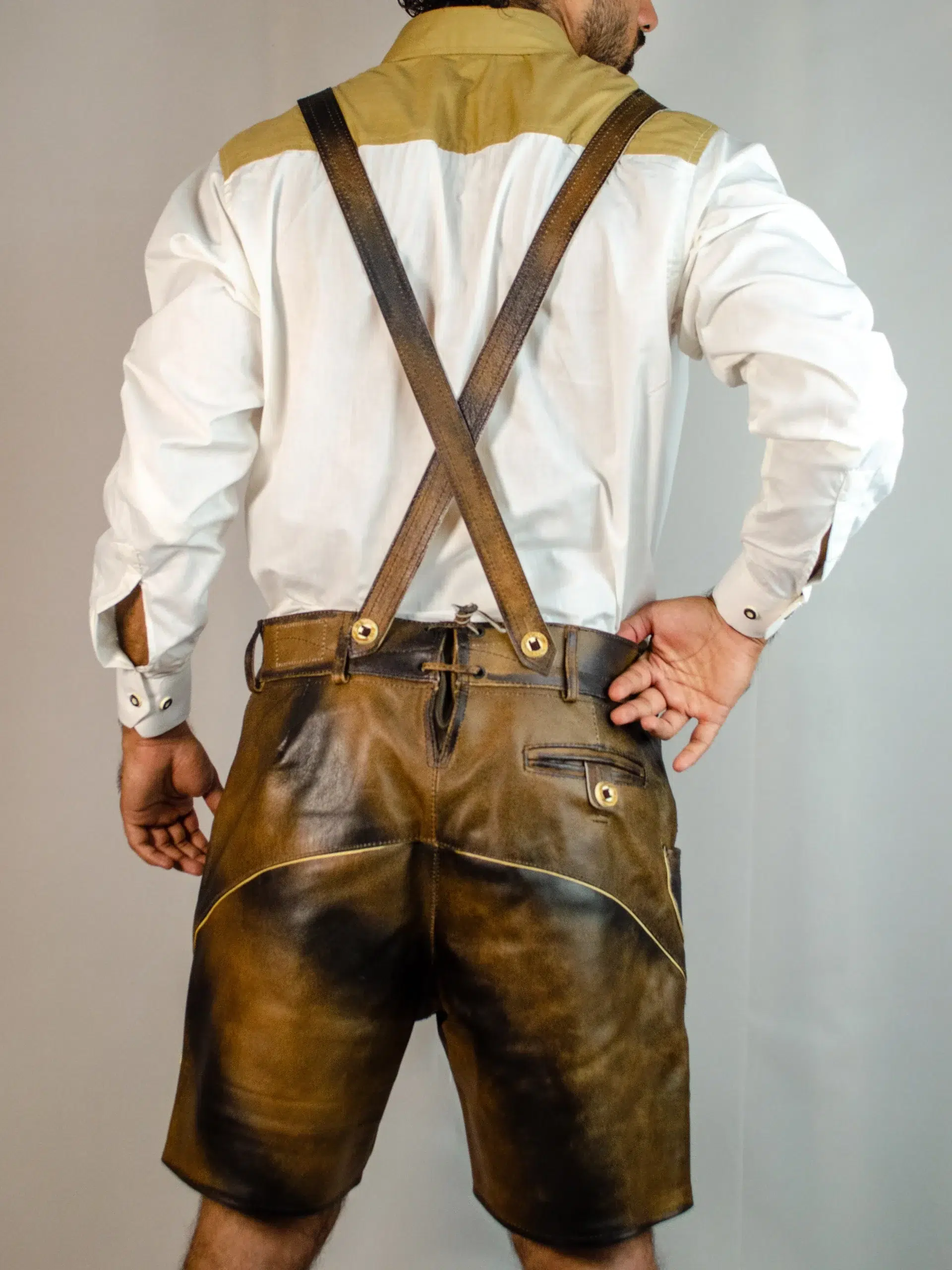 Trachten Short Men Lederhosen Dark Chocolate 5 Back view of a man wearing dark chocolate distressed leather Lederhosen with crossed suspenders and a white shirt with a tan yoke. - Lederhosen For Sale