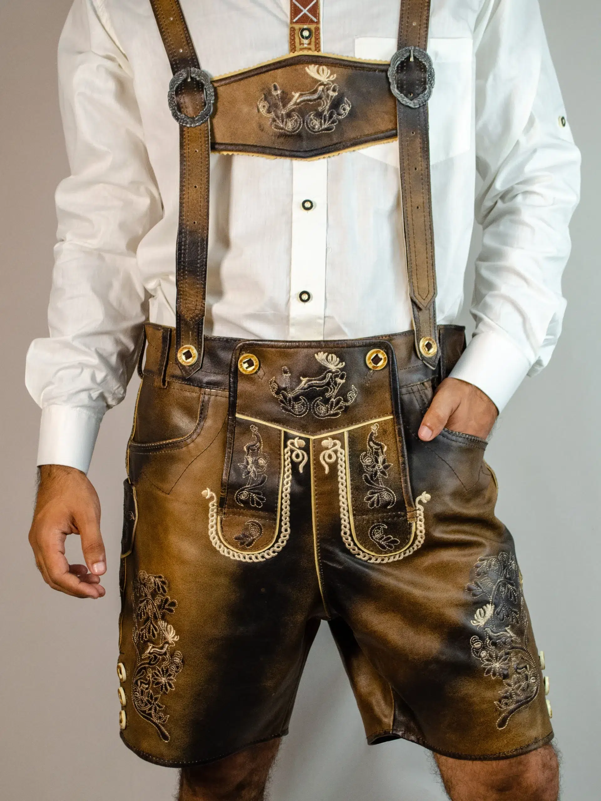 Trachten Short Men Lederhosen Dark Chocolate 3 Front view of a man wearing dark chocolate distressed leather Lederhosen with intricate stag and floral embroidery, matching suspenders, and a white shirt. - Lederhosen For Sale