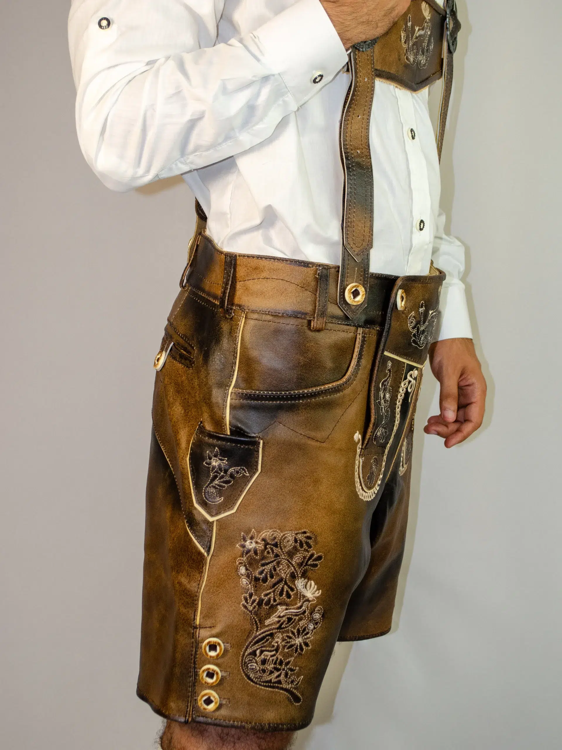 Trachten Short Men Lederhosen Dark Chocolate 2 Side view of a man wearing dark chocolate distressed leather Lederhosen with intricate floral embroidery, matching suspenders, and side horn buttons. - Lederhosen For Sale