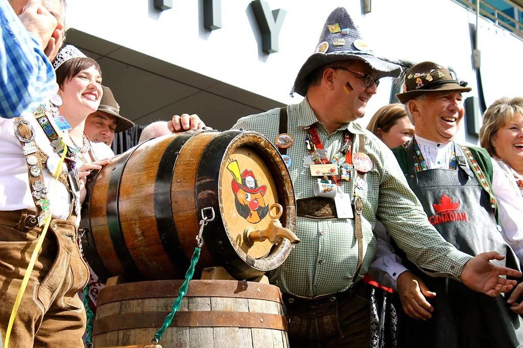 People gathered around a traditional wooden beer barrel at a festive Oktoberfest celebration. - Lederhosen For Sale