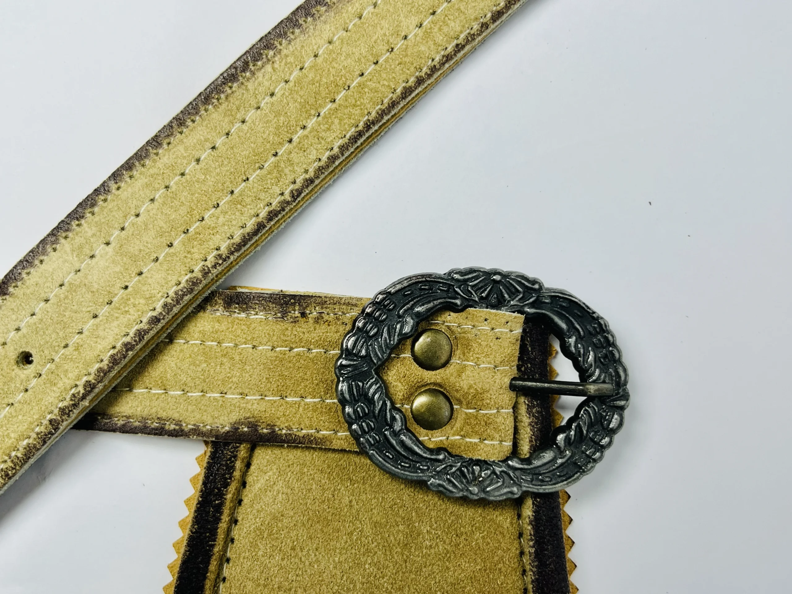 Close-up of a light gold Lederhosen suede suspender strap with an ornate antique silver metal buckle. - Lederhosen For Sale