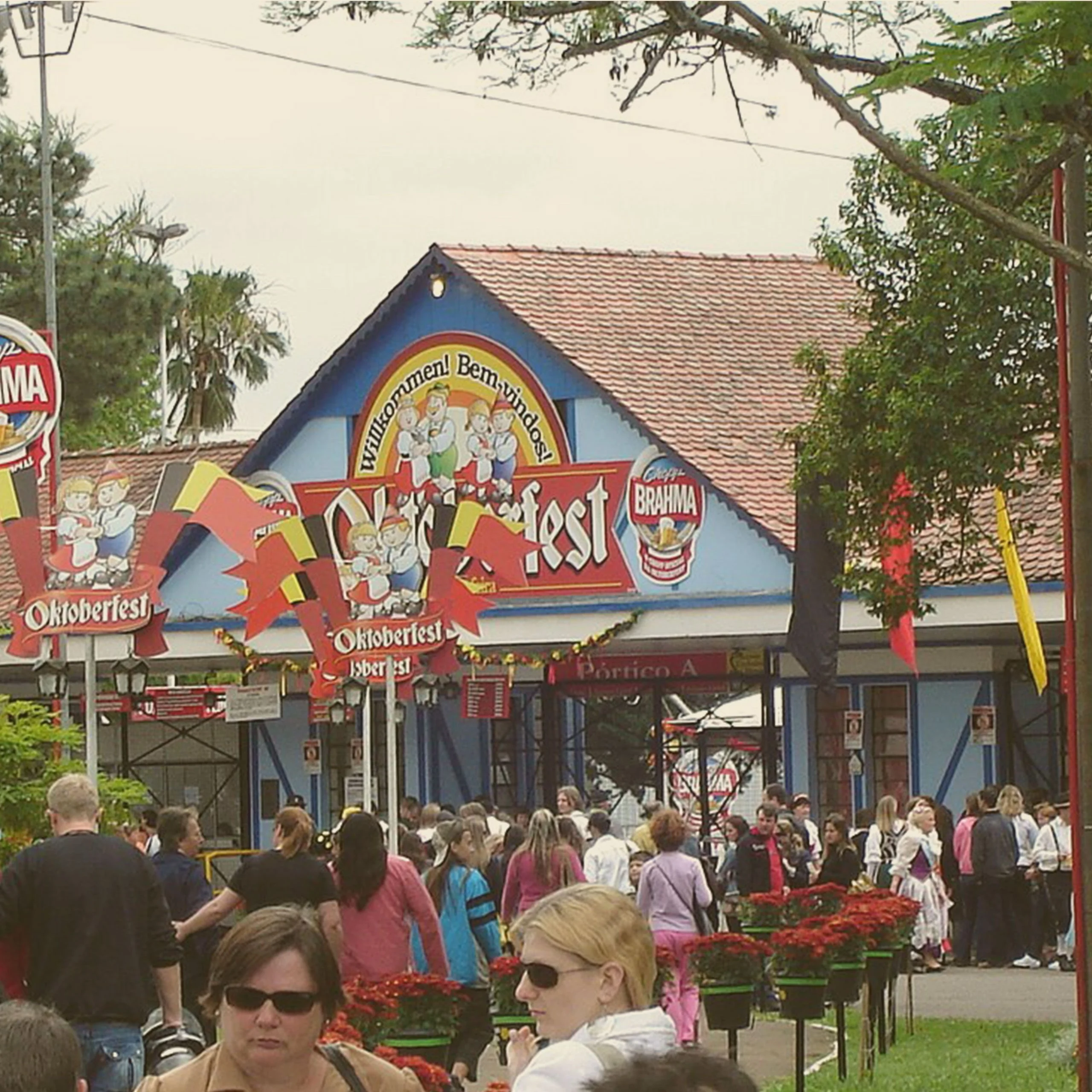 A large crowd of people walking near the main entrance structure of an Oktoberfest festival grounds in Blumenau. - Lederhosen For Sale
