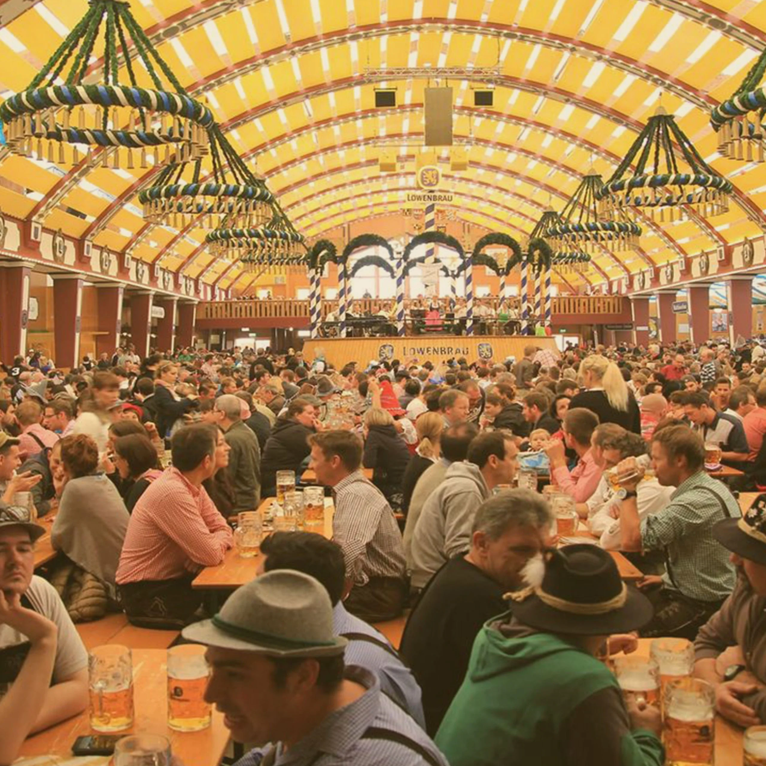 A massive crowd of people sitting at long tables inside a decorated Löwenbräu beer tent during an Oktoberfest celebration in Massachusetts. - Lederhosen For Sale
